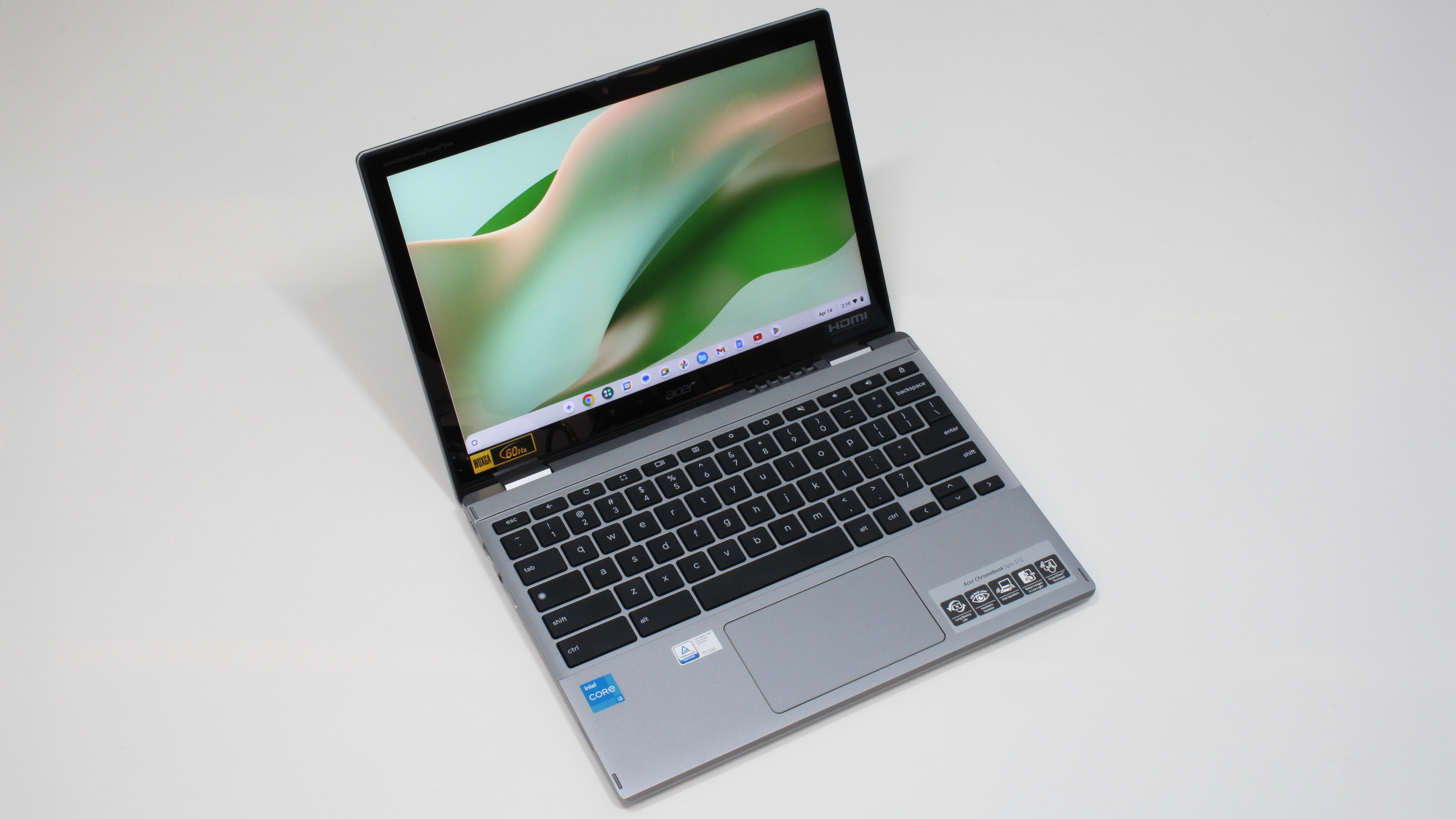 An open and powered on silver laptop with a black keyboard against a white background, showing a curvy green image on its screen.