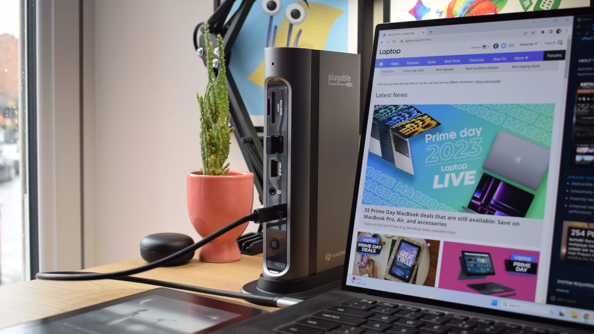 Photo of the Plugable Thunderbolt 4 & USB4 Quad Display Docking Station (TBT4-UDZ) stood vertically with the front-facing Thunderbolt host port connected to a Dell XPS 15 laptop that is showing the Laptop Mag homepage.