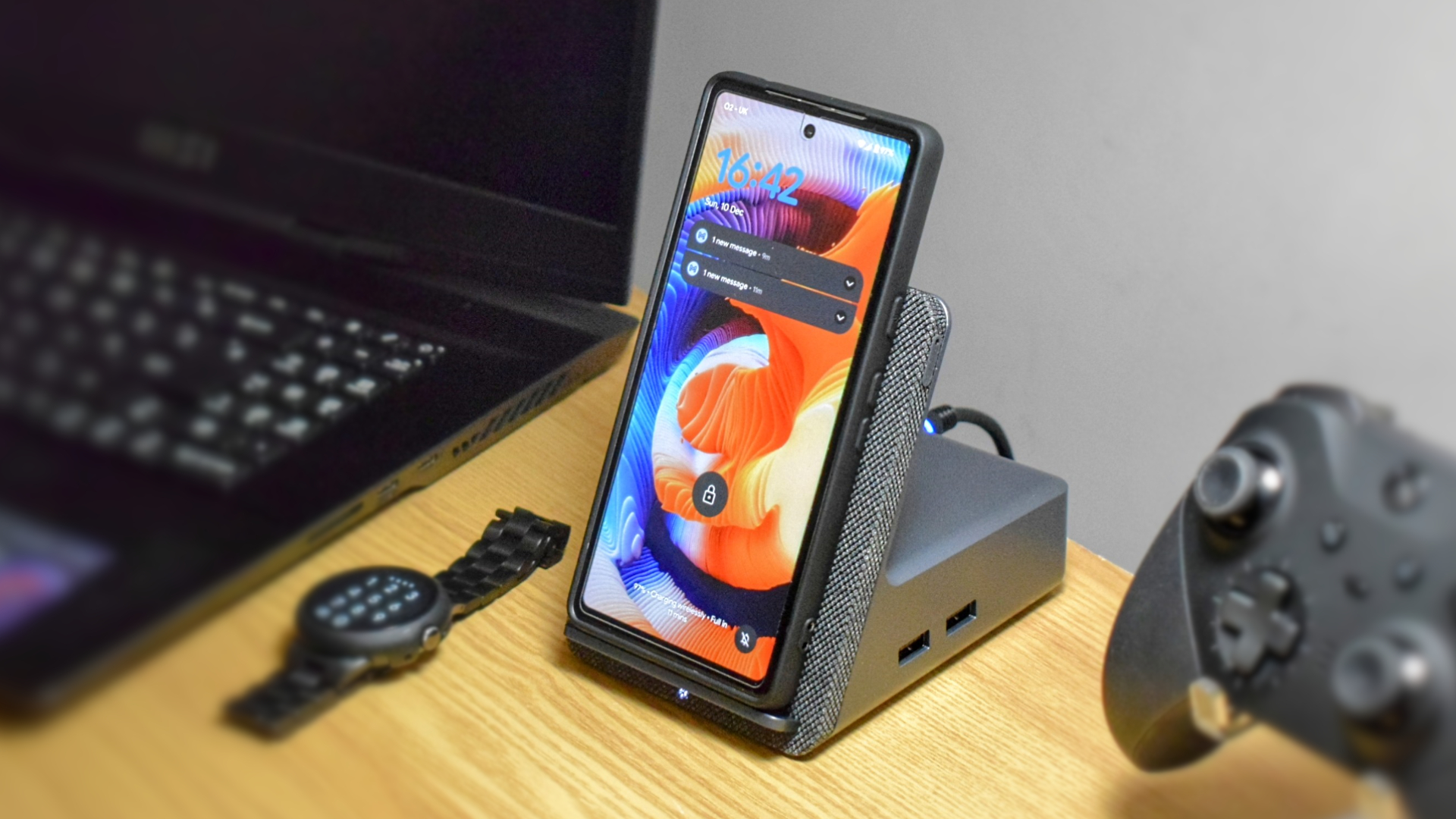 Photo of the Dell Dual Charge Dock with QI wireless charging docking station, showing a Google Pixel 7a in the wireless charging cradle. A Pixel Watch and Xbox Elite Wireless Controller Series 2 are next to the dock.