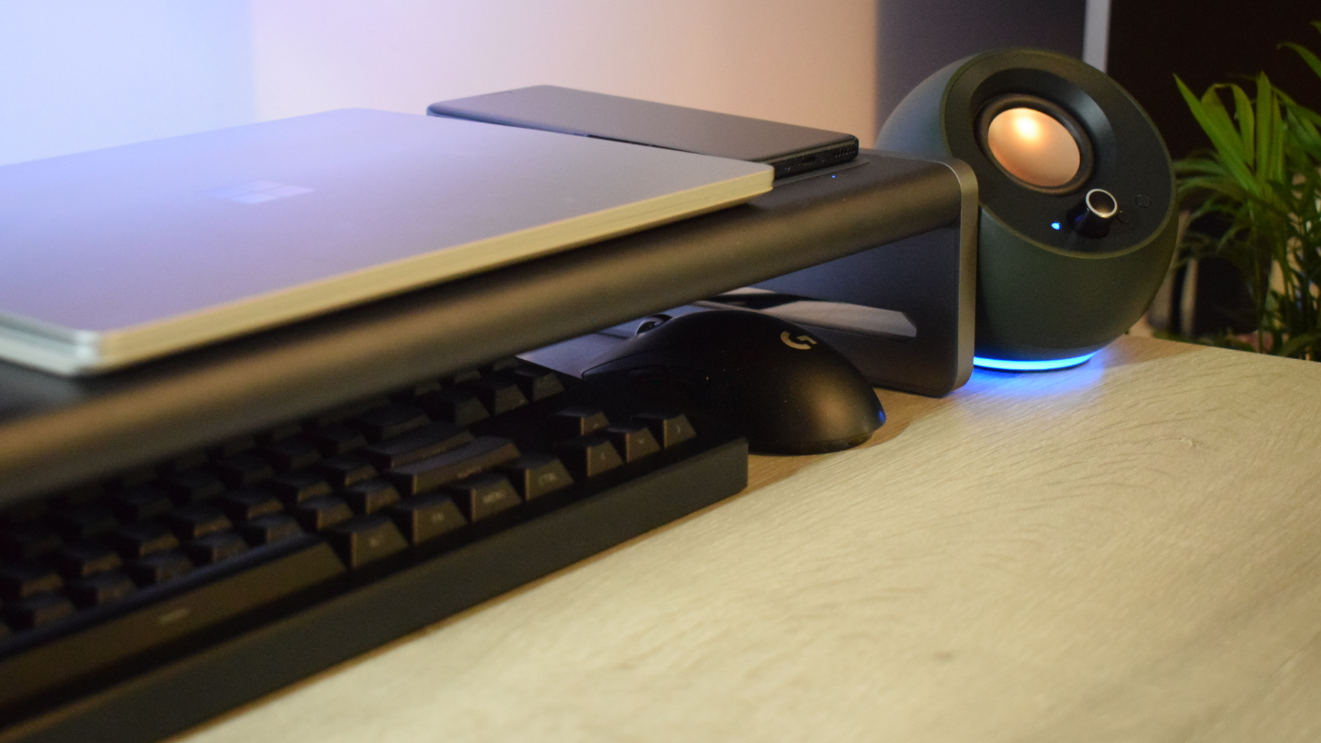 Photo of the Anker 675 USB-C Docking Station as part of a setup showing Creative Pebble speakers, a Microsoft Surface laptop, a Logitech wireless mouse and a wireless keyboard. An Honor Magic5 Pro smartphone is charging on the dock's wireless charging pad.