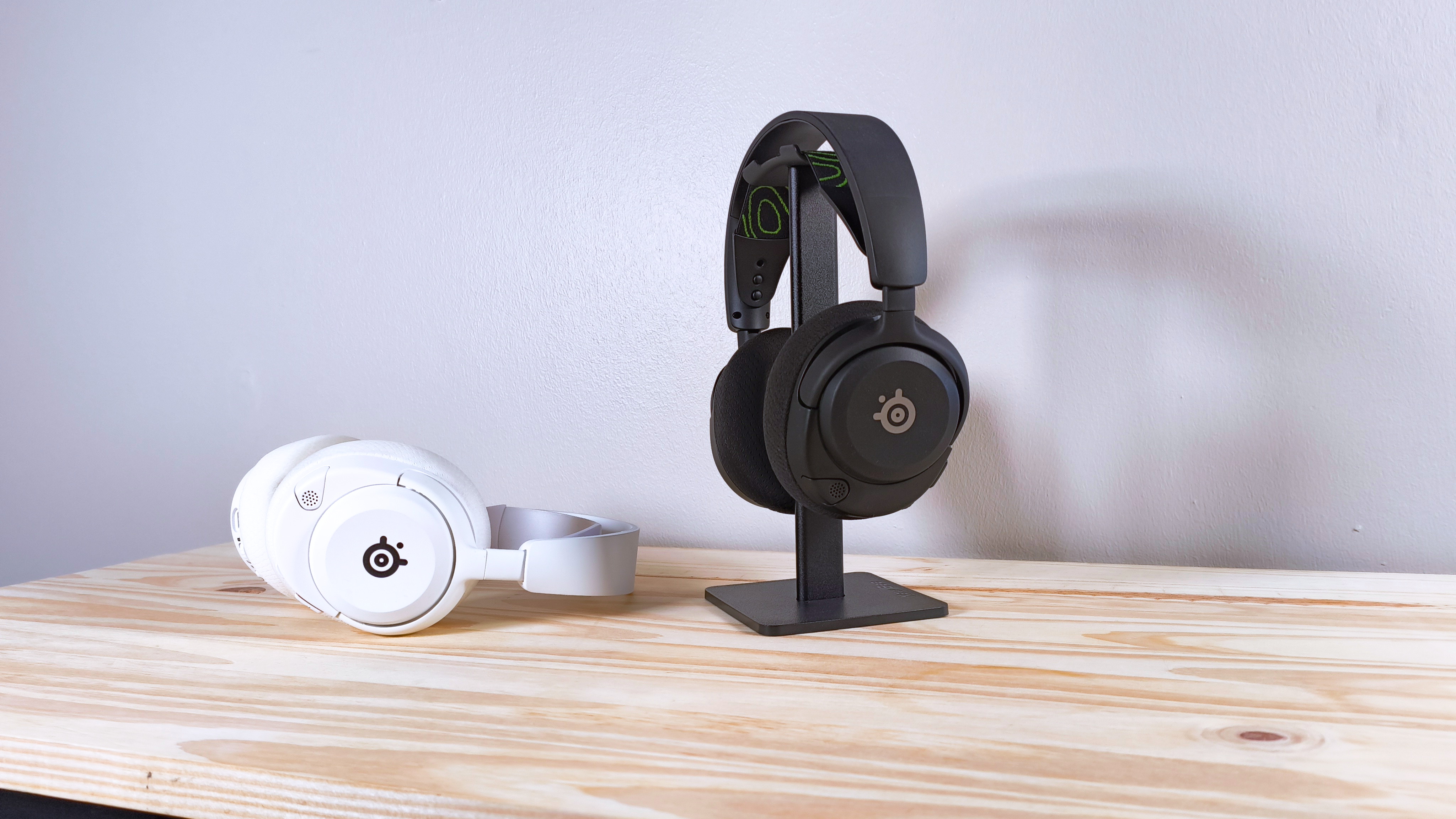 Two pairs of the SteelSeries Arctis Nova 5X in black and white on a wood table