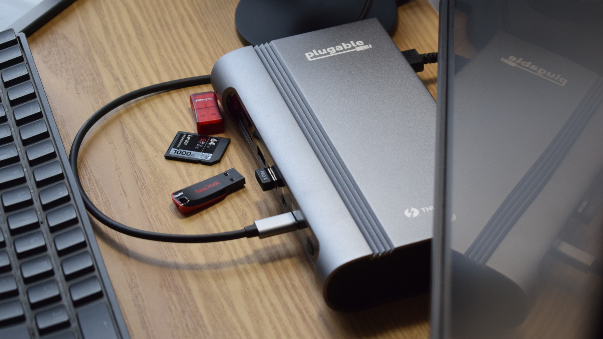 Photo of the Plugable Thunderbolt 4 & USB4 Quad Display Docking Station (TBT4-UDZ) from above, showing the Plugable and Thunderbolt branding with various USB sticks and memory cards.